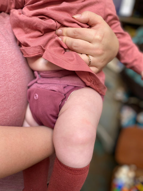 a grown up in pink holds a baby also dressed in pink from head to toe, including their pink cloth diaper